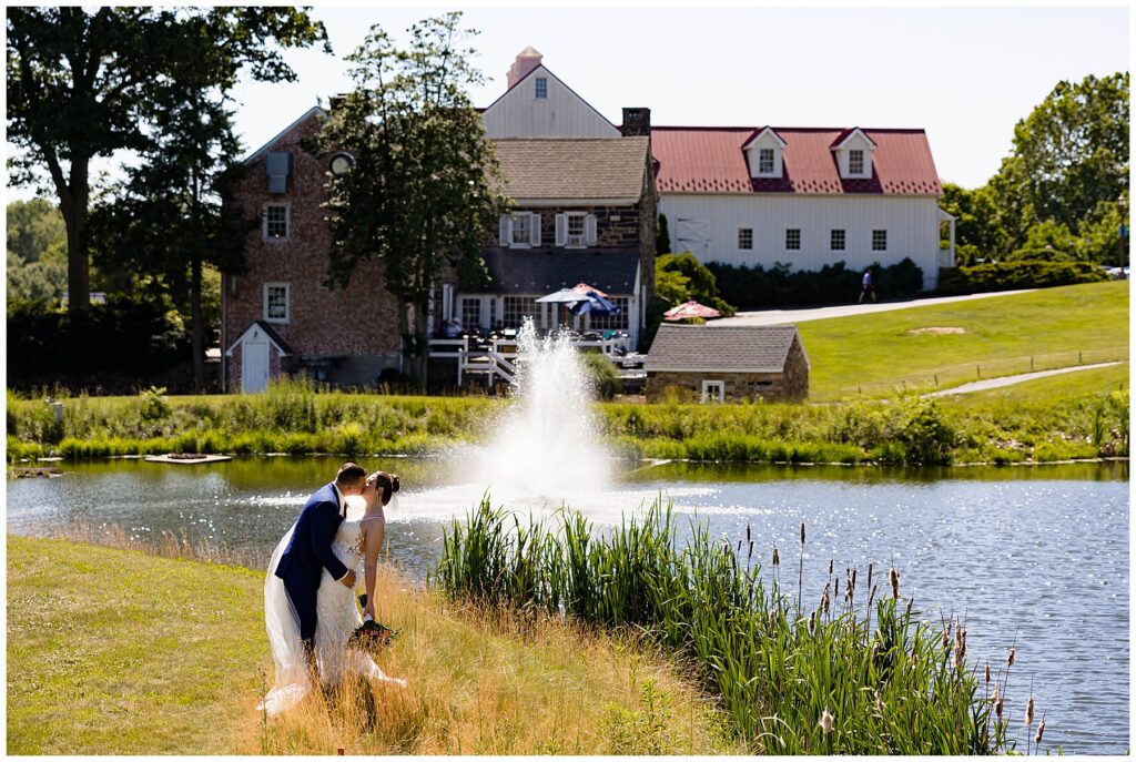 Modern wedding couple performing a dip kiss in the sun in front of a pond at their golf course wedding venue.