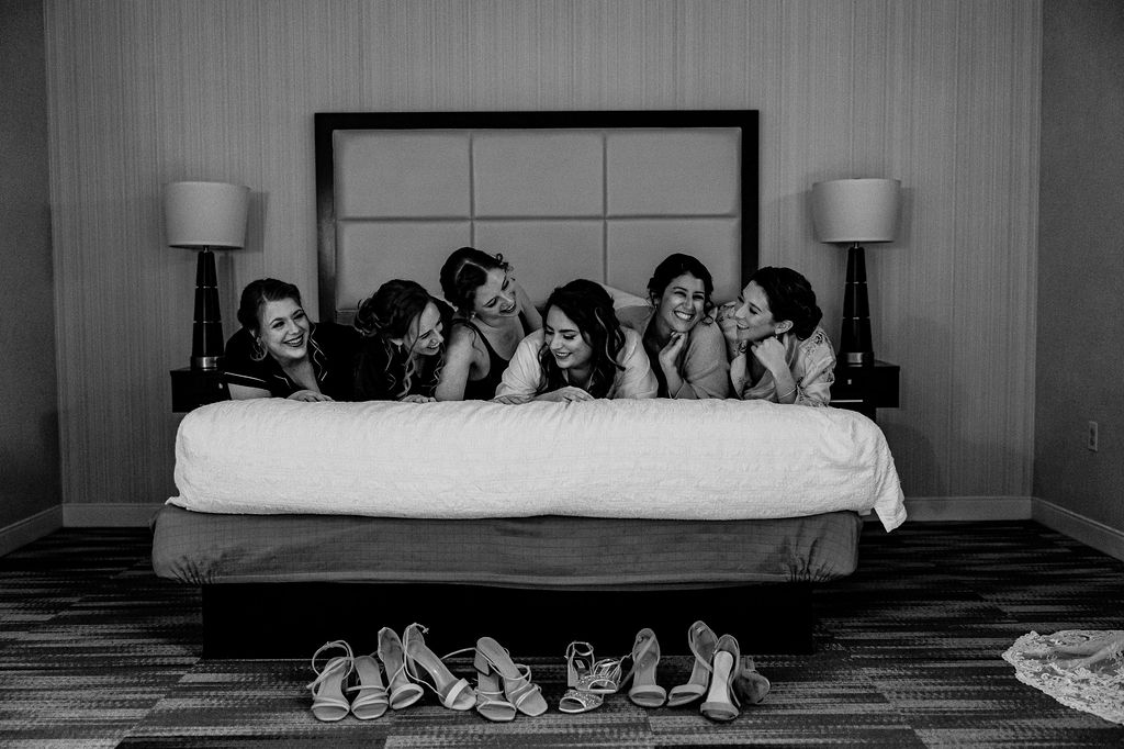 A Bride and Bridesmaids laugh on a bed.