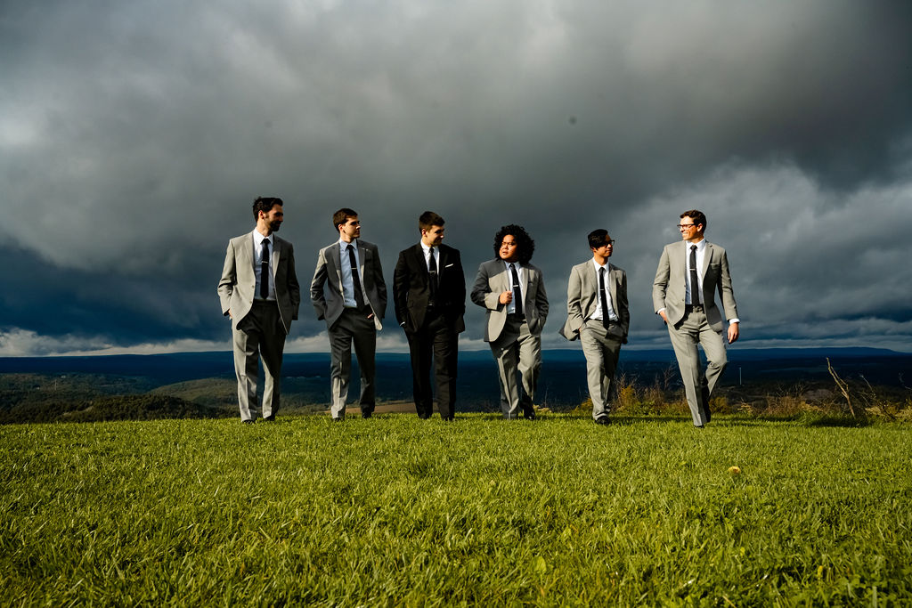 Groomsmen walk in front of clouds with a groom. 