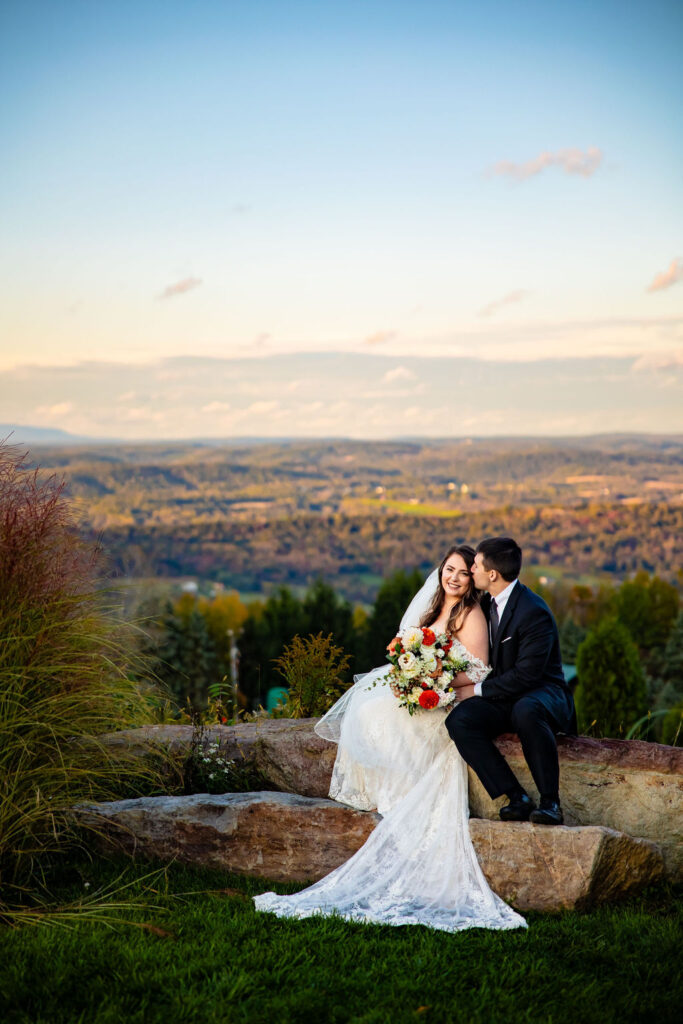 A bride and groom sit overlooking an expanse. 