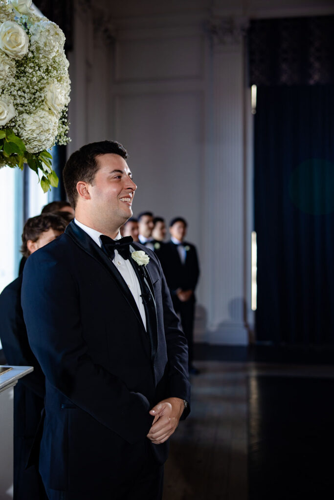 A groom smiles at his bride walking down the aisle. 